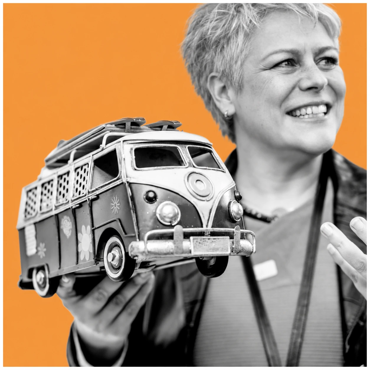 Stefanie Aufleger mit silbergrauer Kurzhaarfrisur hält einen Modellbus – KI-aktualisiertes Originalmotiv vor orangefarbenem Hintergrund.